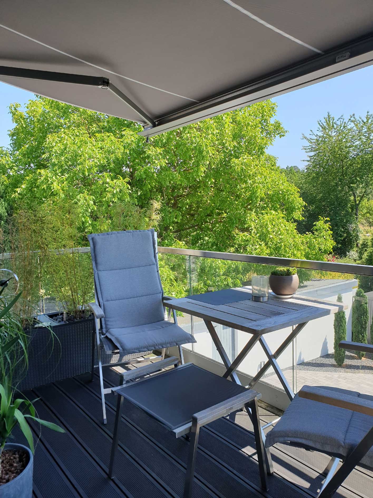 Blick über schattigen Balkon auf den sonnigen Garten - geschützt durch eine Markise